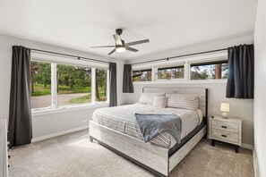 A bedroom with a bed, a ceiling fan, a nightstand with a lamp, and large windows with curtains. - Pikes Peak View  5 Private Acres Game Room (Colorado Springs)