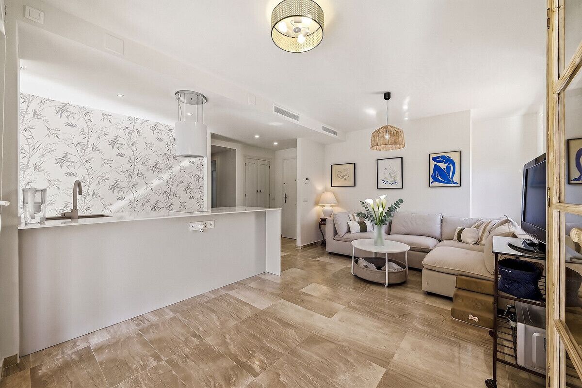 Una sala moderna con un sofá, una mesa de centro y un televisor. Hay una zona de cocina con una encimera y un lavabo.