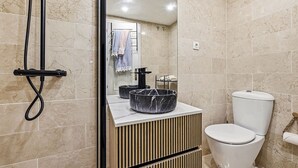 Un bany modern amb un vàter, un lavabo amb una bassina de marbre i una zona de dutxa.