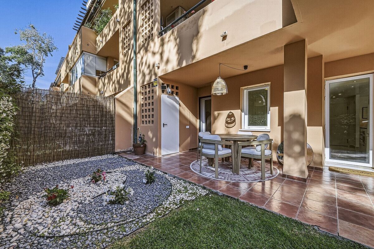 A patio with a table and chairs, a small garden with pebbles and plants, and a building with balconies.
