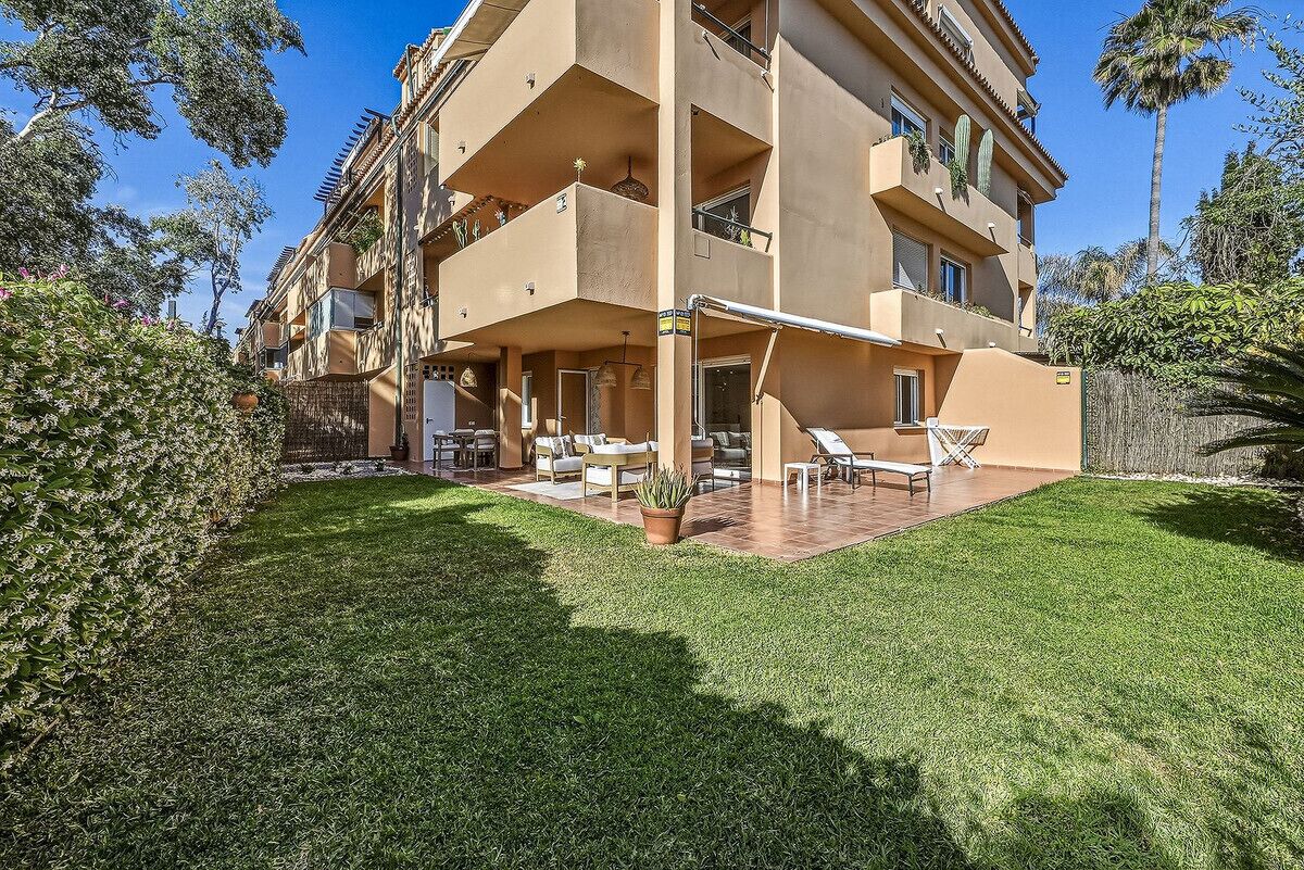 Un edificio de varios pisos con balcones, un patio con mobiliario exterior y un césped bien cuidado.