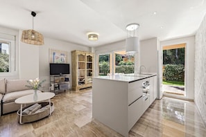 A modern kitchen with a central island, a dining area with a sofa and coffee table, and a television in the living room. - Apartment Alicate Playa by the sea (Marbella)
