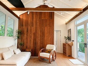 Ein Zimmer mit einer Holzwand, einem weißen Sofa, einem Korbstuhl, einem Holzschrank und einem großen Fenster.