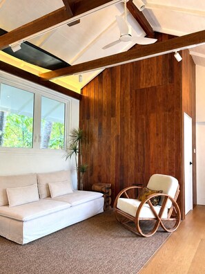 Ein Zimmer mit einem weißen Sofa, einem Korbstuhl, einer Holzverkleidung und einem großen Fenster.