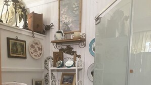 A compact bathroom with a toilet, a small sink, and shelves with various items. - Comfy quaint 1-bedroom cottage with serene pond area in charming Abbeville (Abbeville)