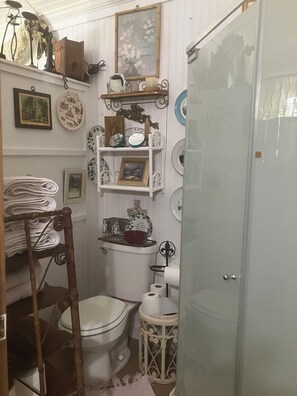 Ein kleines Badezimmer mit Toilette, einem kleinen Waschbecken und Regalen mit verschiedenen Gegenständen.