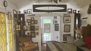 A room with a bed, a sofa, a wooden chest, and a dining table. - Comfy quaint 1-bedroom cottage with serene pond area in charming Abbeville (Abbeville)