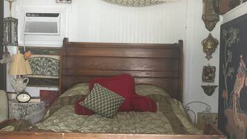 A wooden bed with a headboard, a red pillow, and a patterned bedspread.