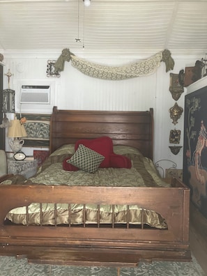 A wooden bed with a headboard, a red pillow, and a patterned bedspread.