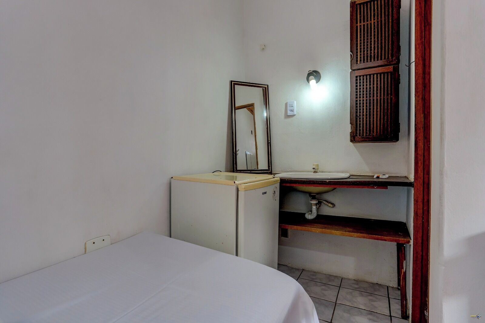 A small, compact room with a single bed, a desk with a chair, a mirror, a sink, and a window with wooden shutters.