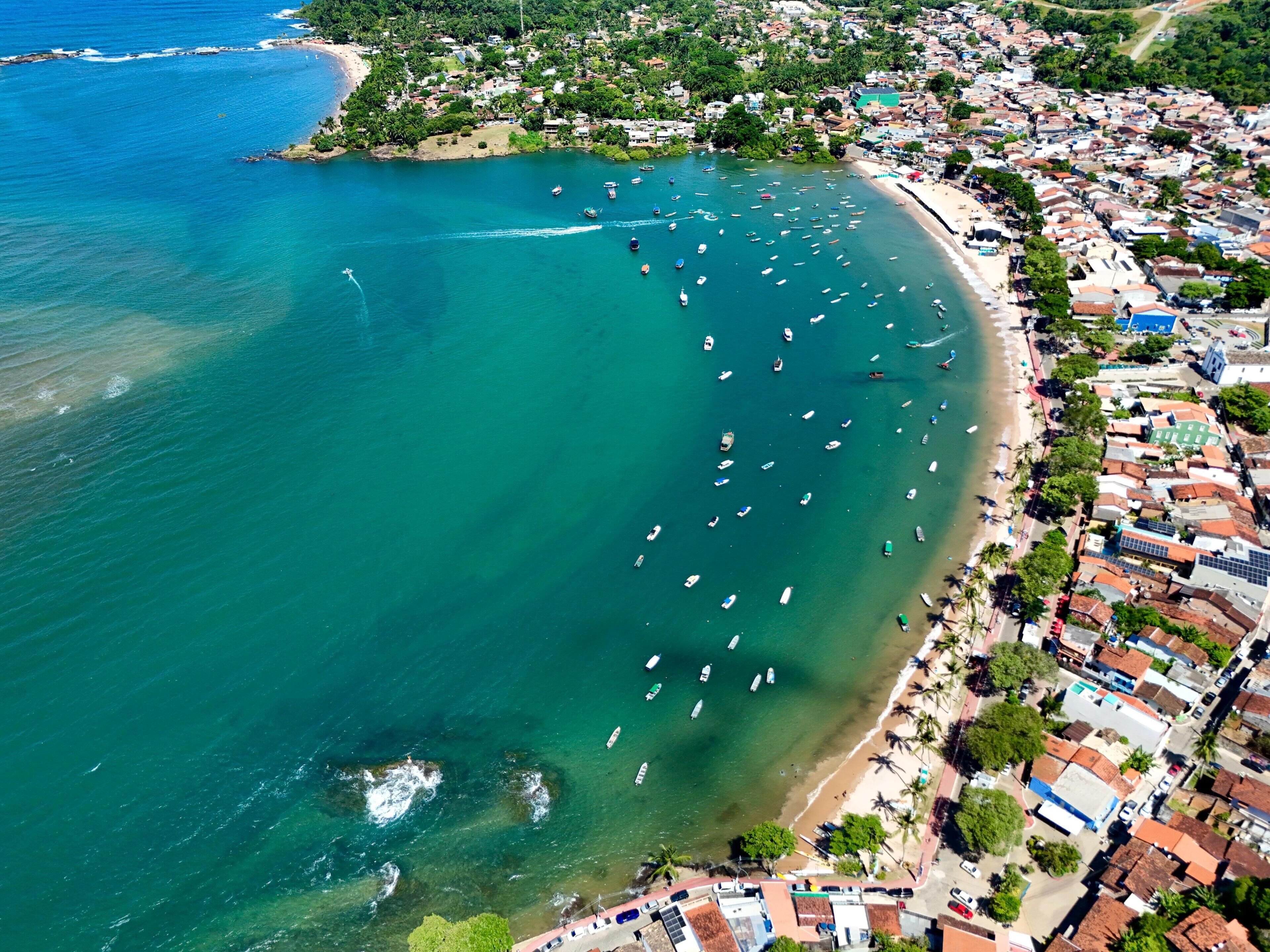 Vista aérea de uma vila costeira com praia, barcos e edifícios residenciais.