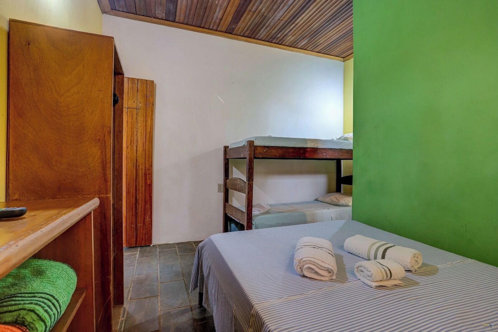 A small, compact room with bunk beds, a wooden wardrobe, a small table, and a green wall.