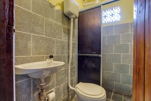 Un baño con lavamanos, inodoro y zona de ducha, con paredes de azulejos y una ventana.