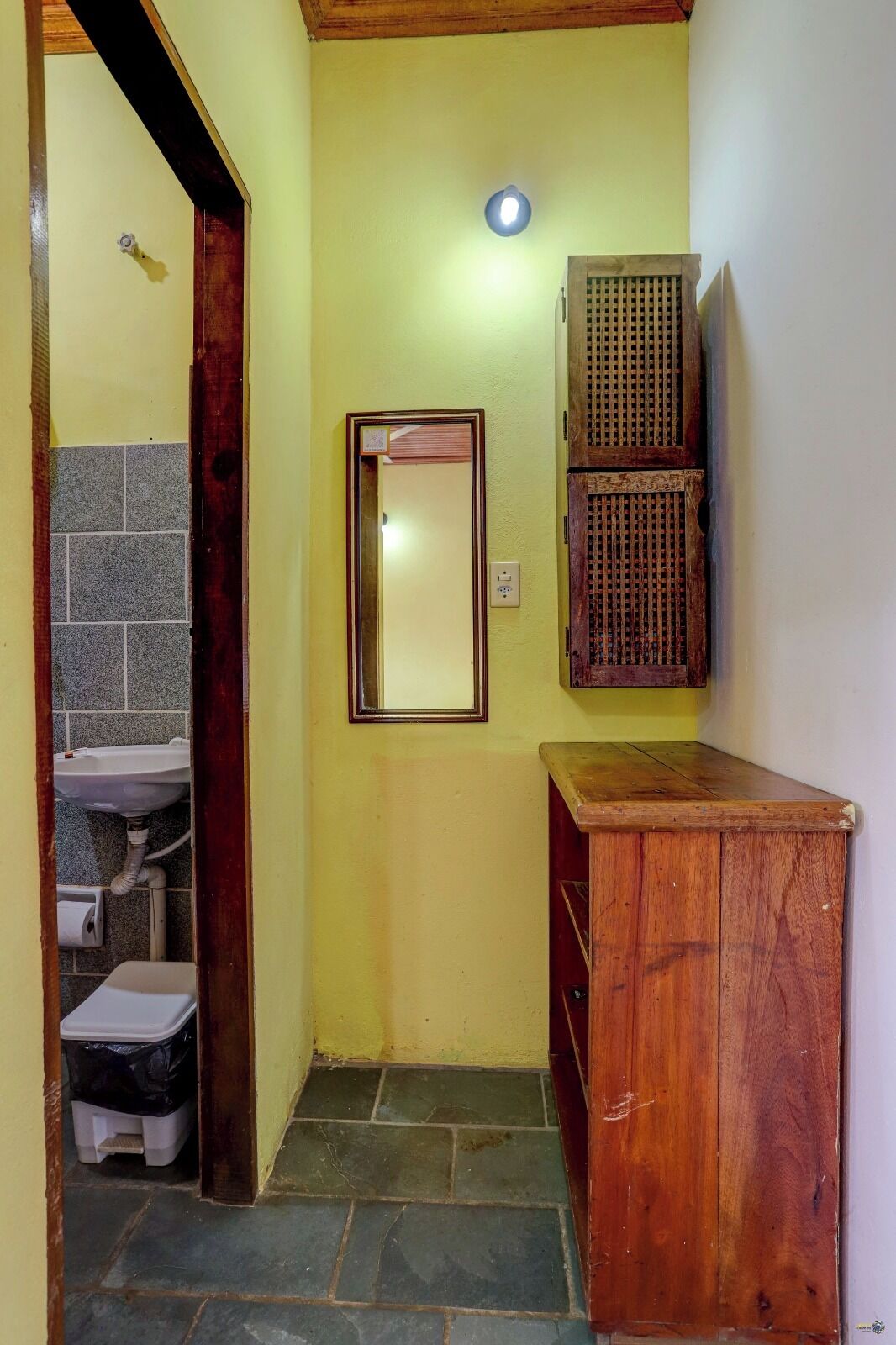 Un couloir étroit avec une armoire en bois, un miroir et un petit lavabo.