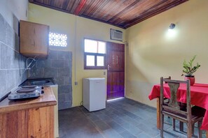 A kitchen with a gas stove, a refrigerator, a wooden cabinet, a window with a decorative grille, and a red table with a chair. - Pousada Pedra Solitária (Itacaré)