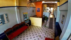 Un pasillo con baldosas estampadas, un banco de madera, un mostrador de recepción y un techo alicatado.