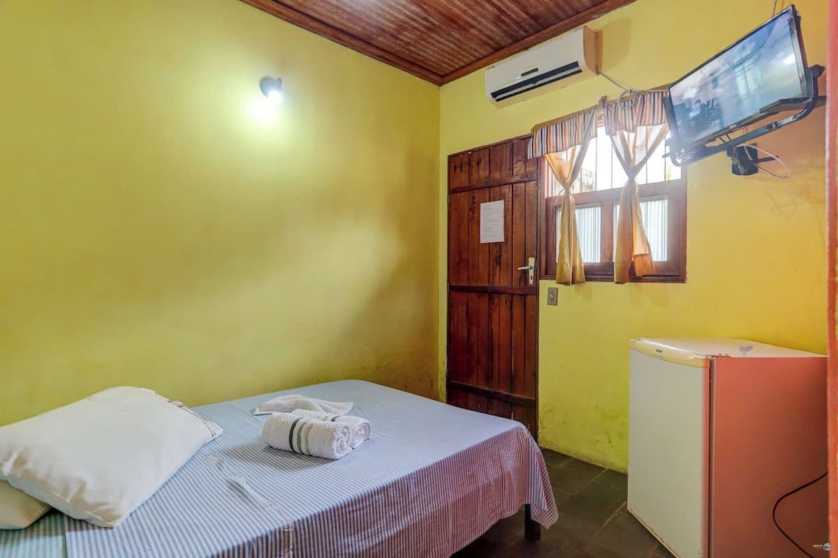 Une petite pièce comprenant un lit, une fenêtre avec des rideaux, un lavabo et un téléviseur fixé au mur.