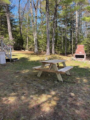 Una mesa de picnic en un área boscosa con un horno de ladrillo.