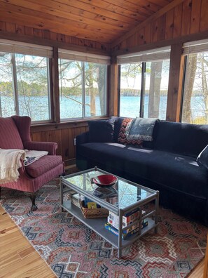 A cozy cabin interior with a wooden ceiling, a blue sofa, a red bowl on a glass coffee table, and a patterned rug. - Cozy, Tranquil Lakefront Retreat (Windham)