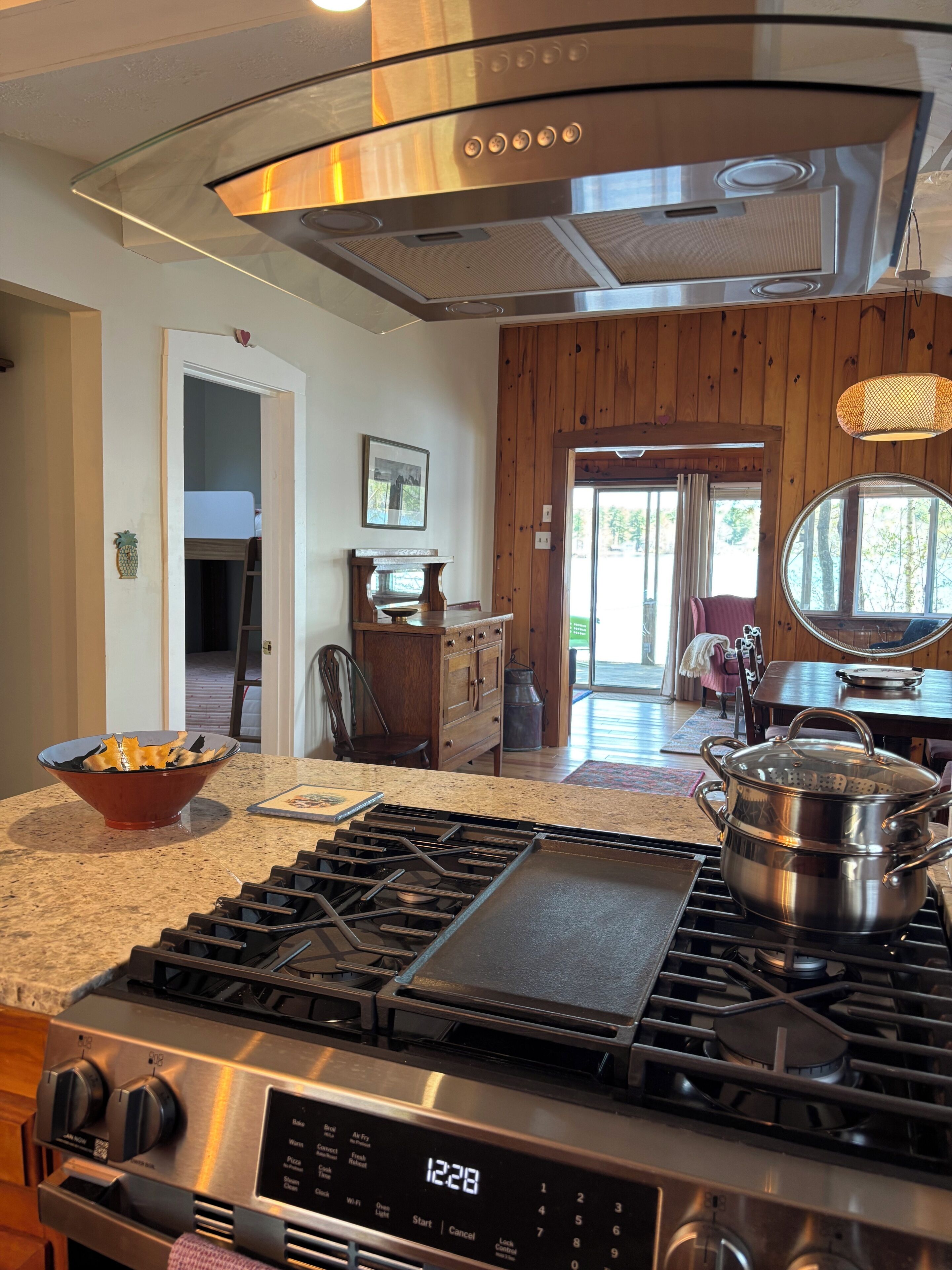 A kitchen with a stainless steel stove, a wooden dining table, and a view of the outdoors.