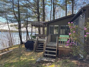 A cabin with a deck, a covered grill, a bench, and a view of a lake. - Cozy, Tranquil Lakefront Retreat (Windham)