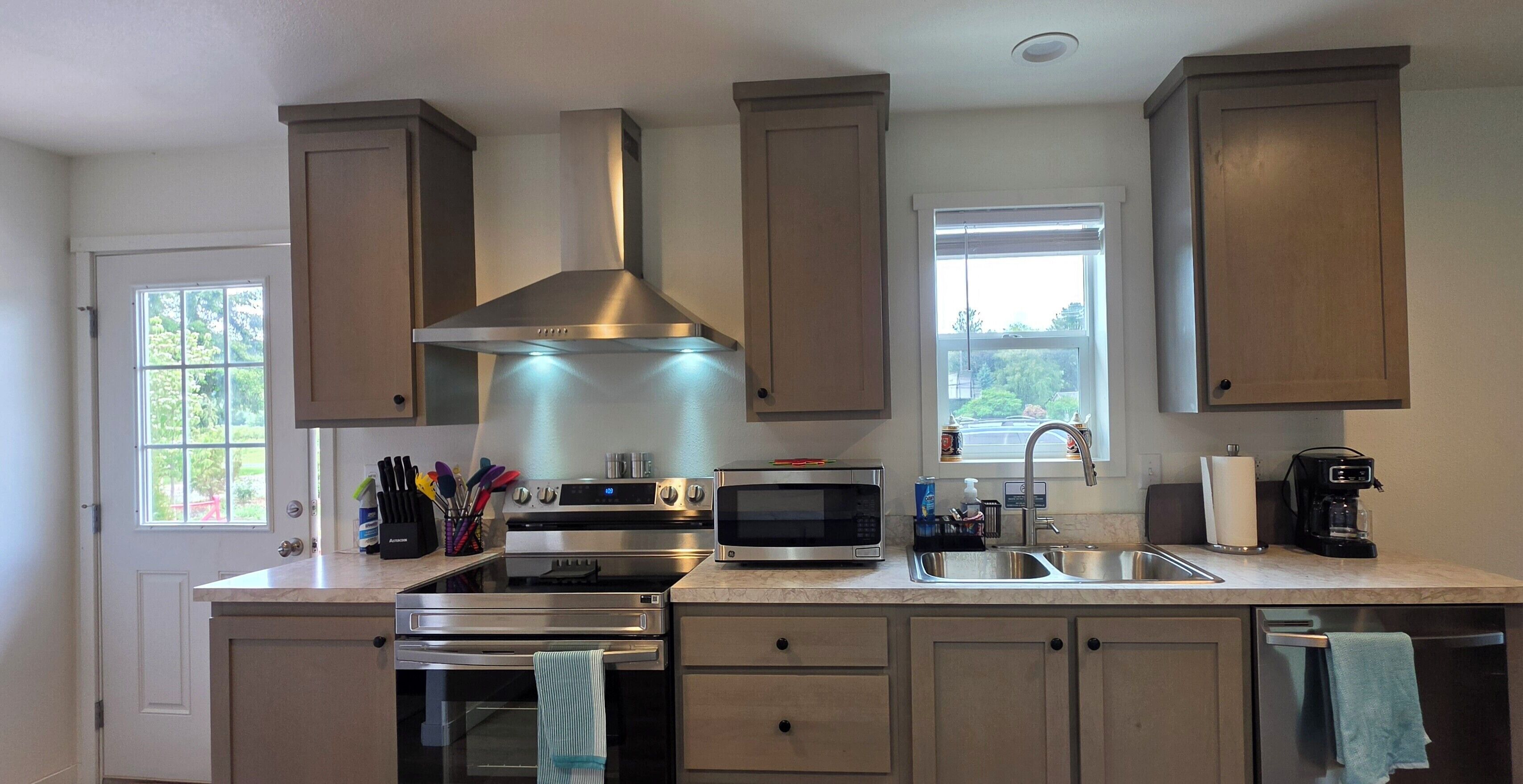 A modern kitchen with stainless steel appliances, a large range hood, and a window with a view of trees.