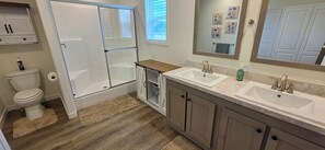 Une salle de bain avec une douche, des toilettes, deux lavabos et un miroir.