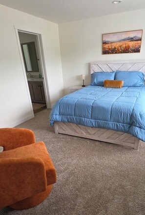 Une chambre à coucher avec un lit, un tableau, une chaise et une porte donnant sur une salle de bain.