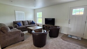 A living room with a sectional sofa, a coffee table, two leather ottomans, a flat-screen TV, and a door with a window. - Beautiful 3-bedroom home in rural Mossyrock.  Close to recreational activities. (Mossyrock)