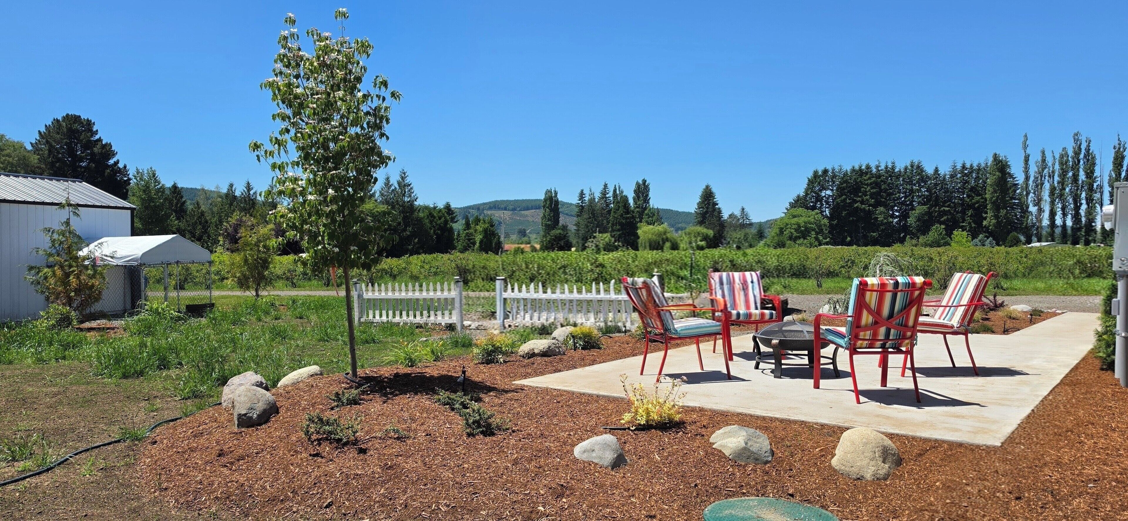 An outdoor patio with chairs and a table, surrounded by a landscaped garden with mulch and rocks.