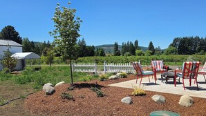 An outdoor patio with chairs and a table, surrounded by a landscaped garden with mulch and rocks. - Beautiful 3-bedroom home in rural Mossyrock.  Close to recreational activities. (Mossyrock)