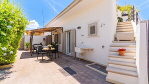 A patio with a table and chairs, a covered seating area, a staircase, and a white wall with a window and a sink. - Holiday Home 'Marcella' with Private Terrace, Private Garden and Air Conditioning (Torre Lapillo)