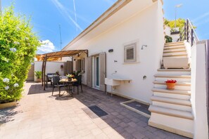 A patio with a table and chairs, a covered seating area, a staircase, and a white wall with a window and a sink. - Holiday Home 'Marcella' with Private Terrace, Private Garden and Air Conditioning (Torre Lapillo)