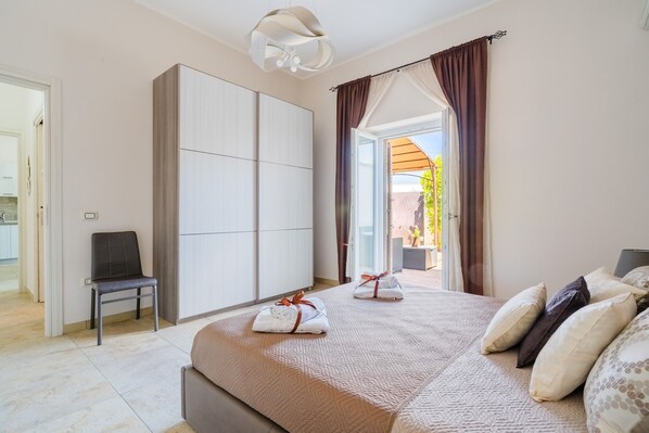 A hotel room with a bed, a chair, a wardrobe, and a view of the outdoors.