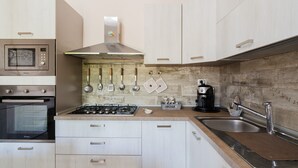 A modern kitchen with a microwave, oven, stove, and stainless steel sink. - Holiday Home 'Marcella' with Private Terrace, Private Garden and Air Conditioning (Torre Lapillo)
