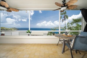 Un balcon avec vue sur la mer, un ventilateur de plafond et une table avec des chaises.