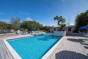Une piscine avec une terrasse en bois, des chaises longues et des parasols.