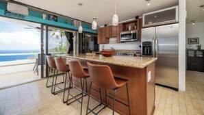 A kitchen with a large island, bar stools, a refrigerator, and a view of the ocean. - Brand New Centrally Located  2BD/1BA Ocean View (St. Thomas)