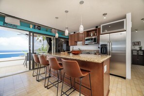 A kitchen with a large island, bar stools, a refrigerator, and a view of the ocean. - Brand New Centrally Located  2BD/1BA Ocean View (St. Thomas)