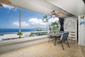 Een balkon met een tafel en stoelen, een plafondventilator en uitzicht op de oceaan.