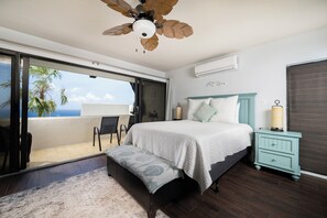 Une chambre à coucher comprenant un lit, une table de chevet, un banc, un ventilateur de plafond et une vue sur l’océan.
