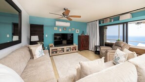 A living room with a sofa, a television, a ceiling fan, and a view of the ocean. - Brand New Centrally Located  2BD/1BA Ocean View (St. Thomas)
