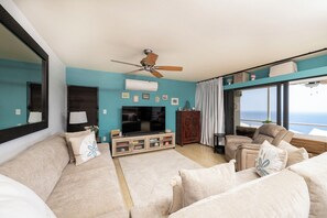 A living room with a sofa, a television, a ceiling fan, and a view of the ocean. - Brand New Centrally Located  2BD/1BA Ocean View (St. Thomas)