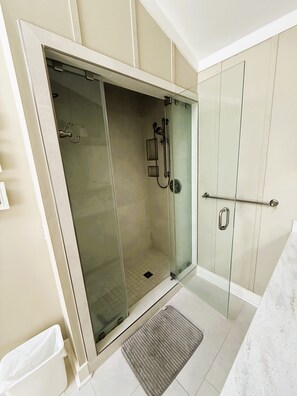 Una cabina doccia con pareti in vetro, soffione a mano e pavimento piastrellato.