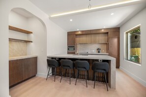 Una cocina moderna con una isla central, taburetes de bar, armarios de madera y un ventanal grande.