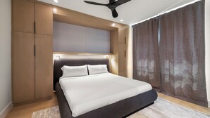 A modern bedroom with a bed, built-in wardrobe, ceiling fan, and large window with curtains. - The O'Four Collection - The Noir (Houston)