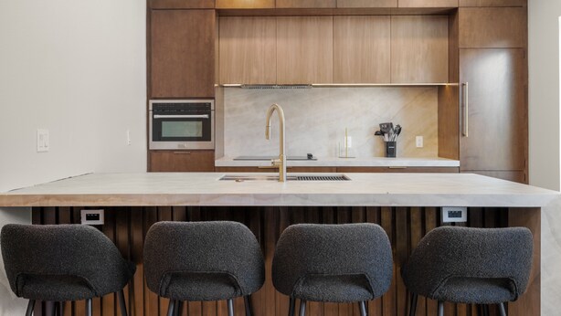 A modern kitchen with a central island, built-in oven, and a stainless steel range hood. - The O'Four Collection - The Noir (Houston)