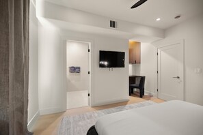 Una habitación de hotel moderna con una cama, un escritorio, una silla, un televisor de pantalla plana y una puerta que conduce a otra habitación.