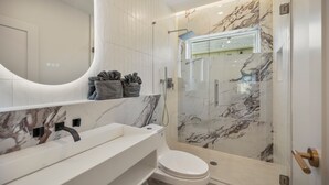 A modern bathroom with a marble sink, toilet, and a glass-enclosed shower. - The O'Four Collection - The Noir (Houston)