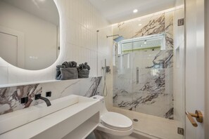 Un baño moderno con lavamanos, inodoro y ducha con cerramiento de vidrio de mármol.